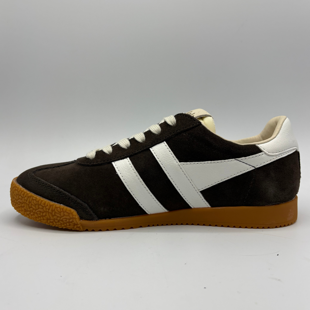 A low-top sneaker in dark brown suede with two wide white side stripes, white laces, a cream collar lining, and a textured brown gum sole, shown in profile against a neutral gray background.