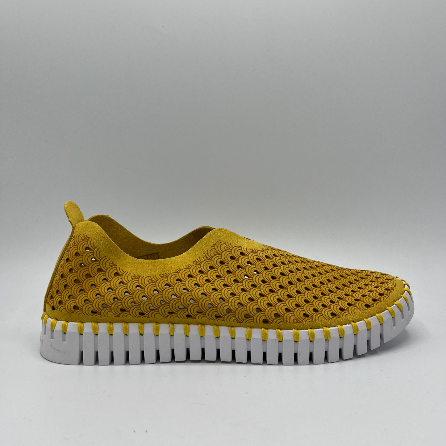 Right facing view of golden rod coloured slip on shoe with an intricate laser cut upper and white rubber outsole.