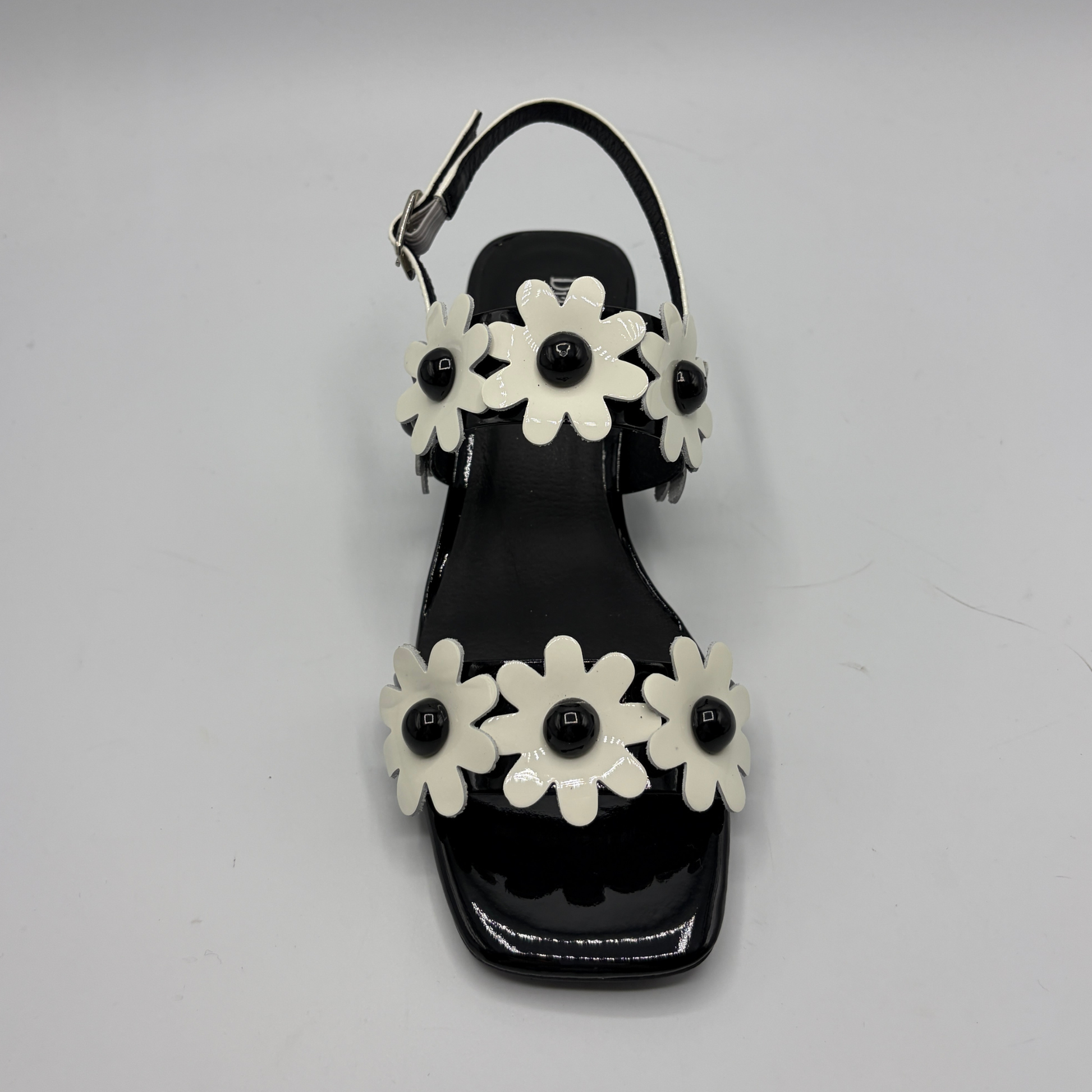 Black sandal with white flower decorations on a gray background