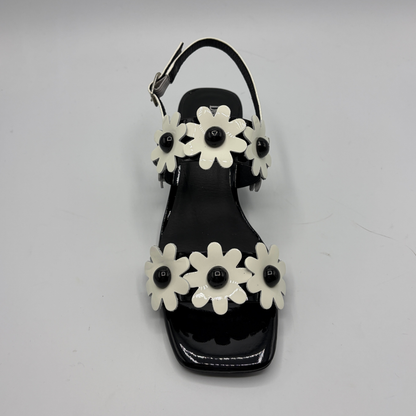 Black sandal with white flower decorations on a gray background