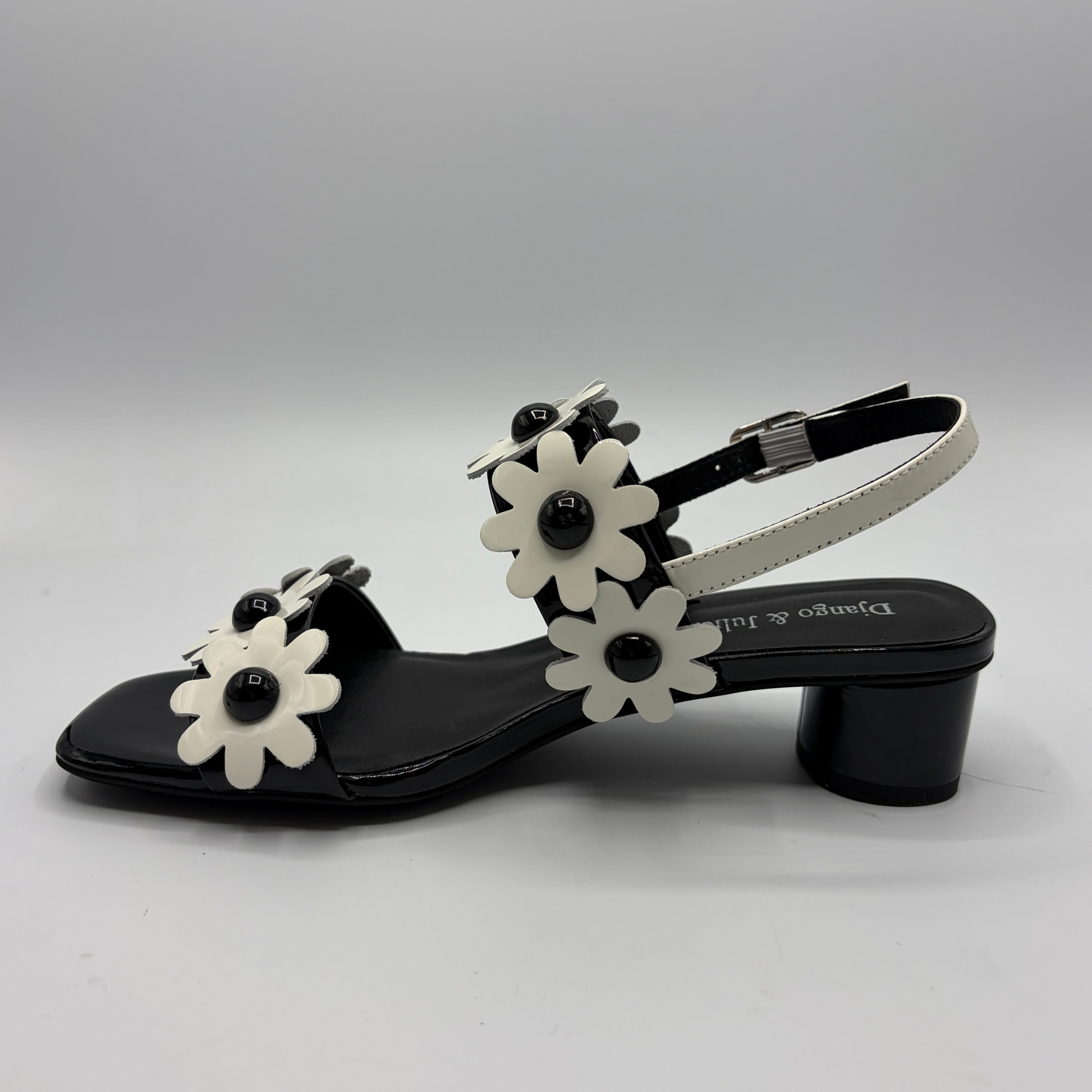 Black sandal with white floral decorations on a gray background