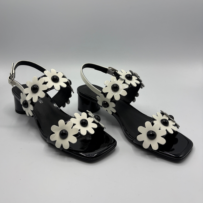 Black sandals with white flower decorations on a gray background