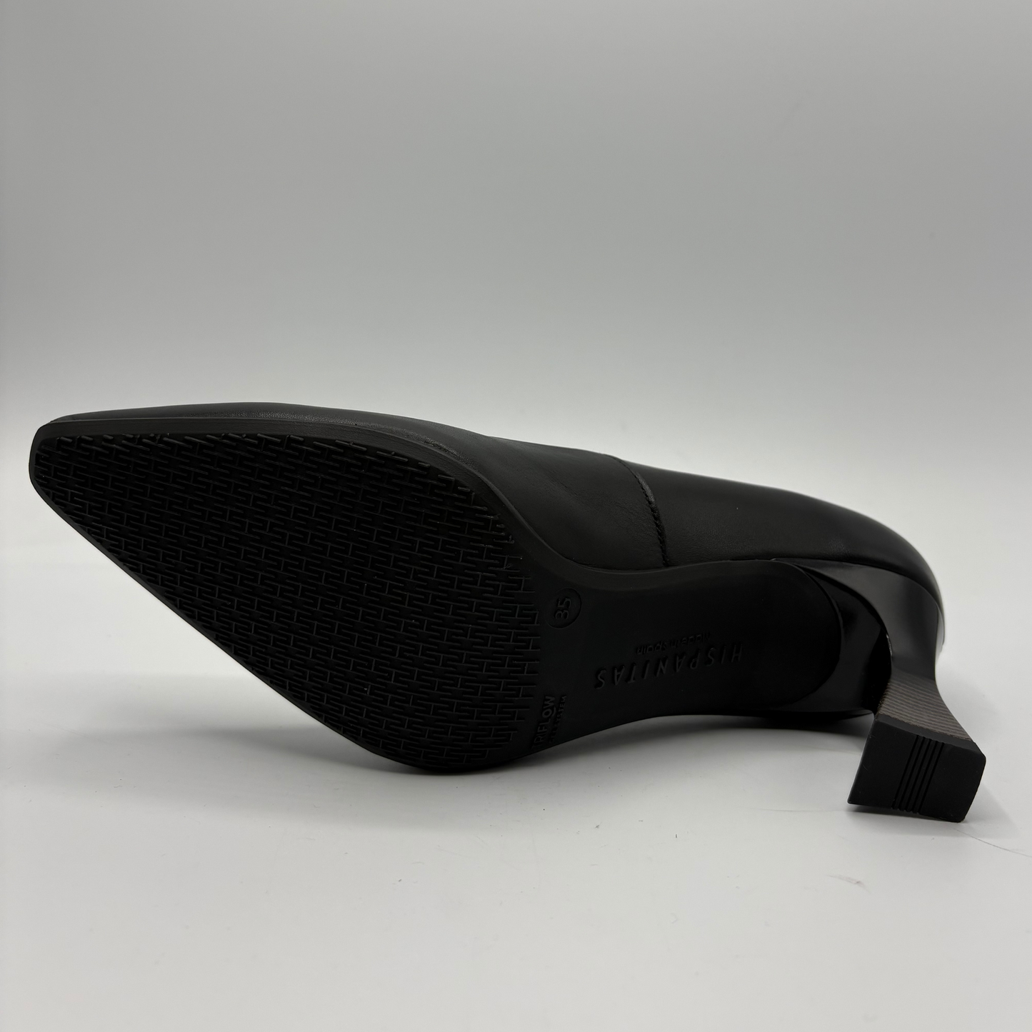 A black pointed-toe high heel shoe shown from a side angle, displaying its textured rubber outsole and block heel on a light gray background.