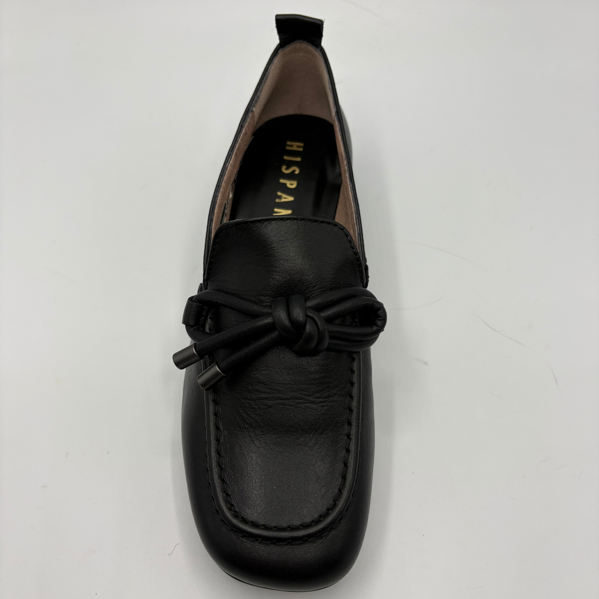 A black leather loafer with a knotted bow detail on the toe, photographed from a top-down angle on a light gray background. The brand name 'HISPANITAS' is visible in gold lettering on the inner sole.