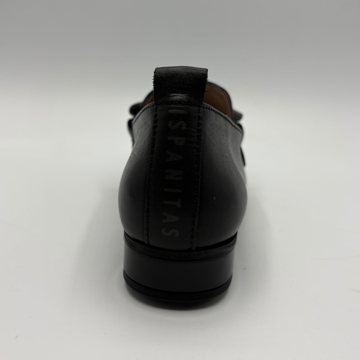 A black leather loafer shown from the back, featuring a pull tab with the brand name 'HISPANITAS' printed vertically in black.