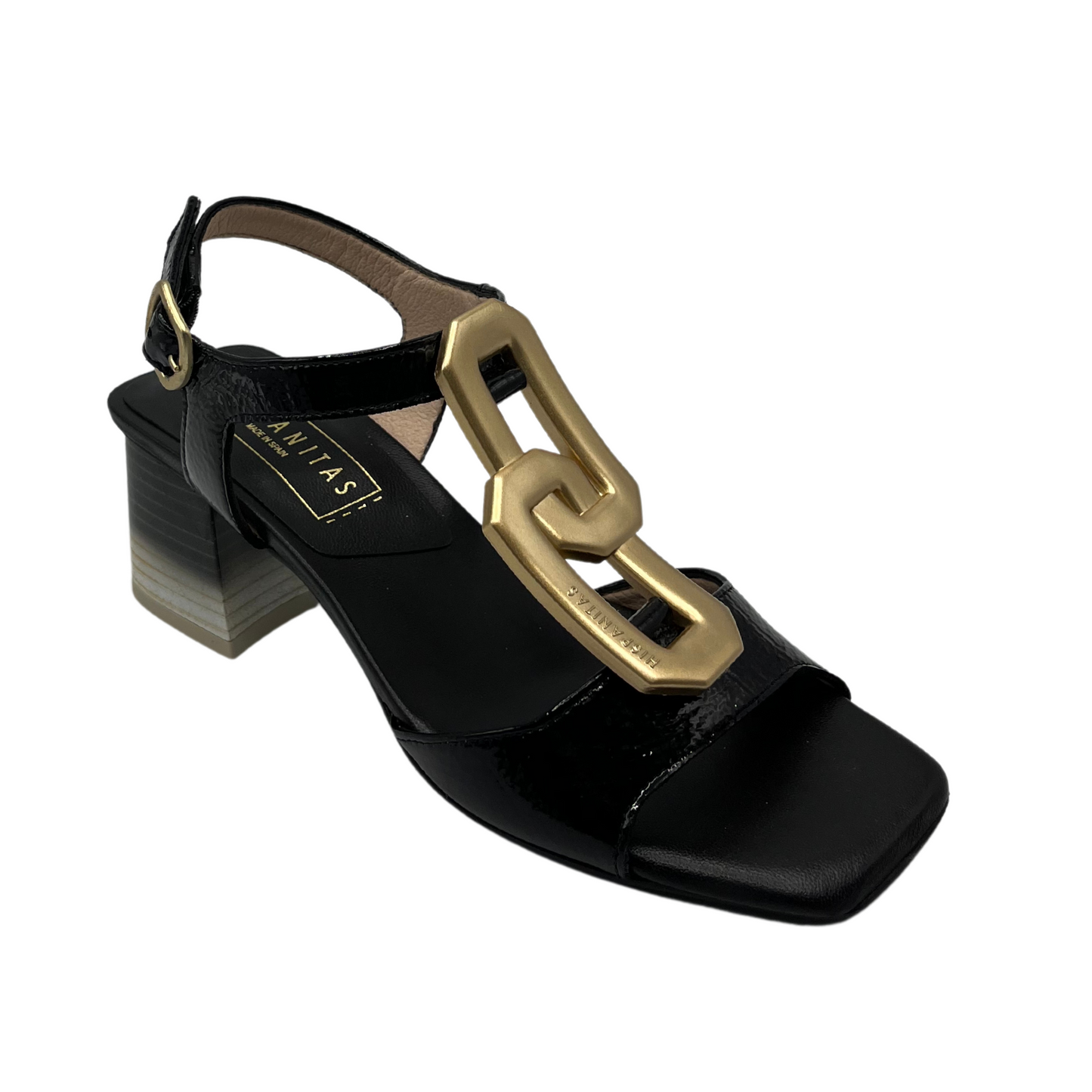 45 degree angled view of black and gold sandal with patent leather and gold brooch detail on upper