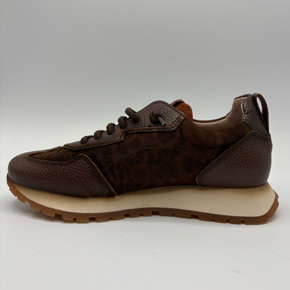 A brown leather sneaker with a textured pebbled upper, matching brown laces, and a thick beige midsole, shown in a side profile against a neutral gray background.