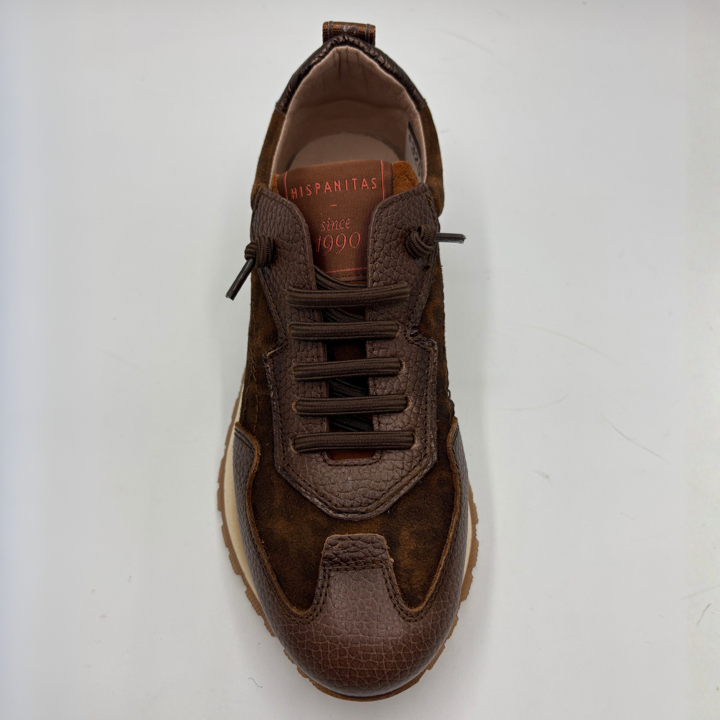 A brown suede and textured leather sneaker shown from a top-down view on a light gray background. The shoe features matching brown laces, a textured toe cap, and a tan interior lining with 'HISPANITAS' printed on the insole.