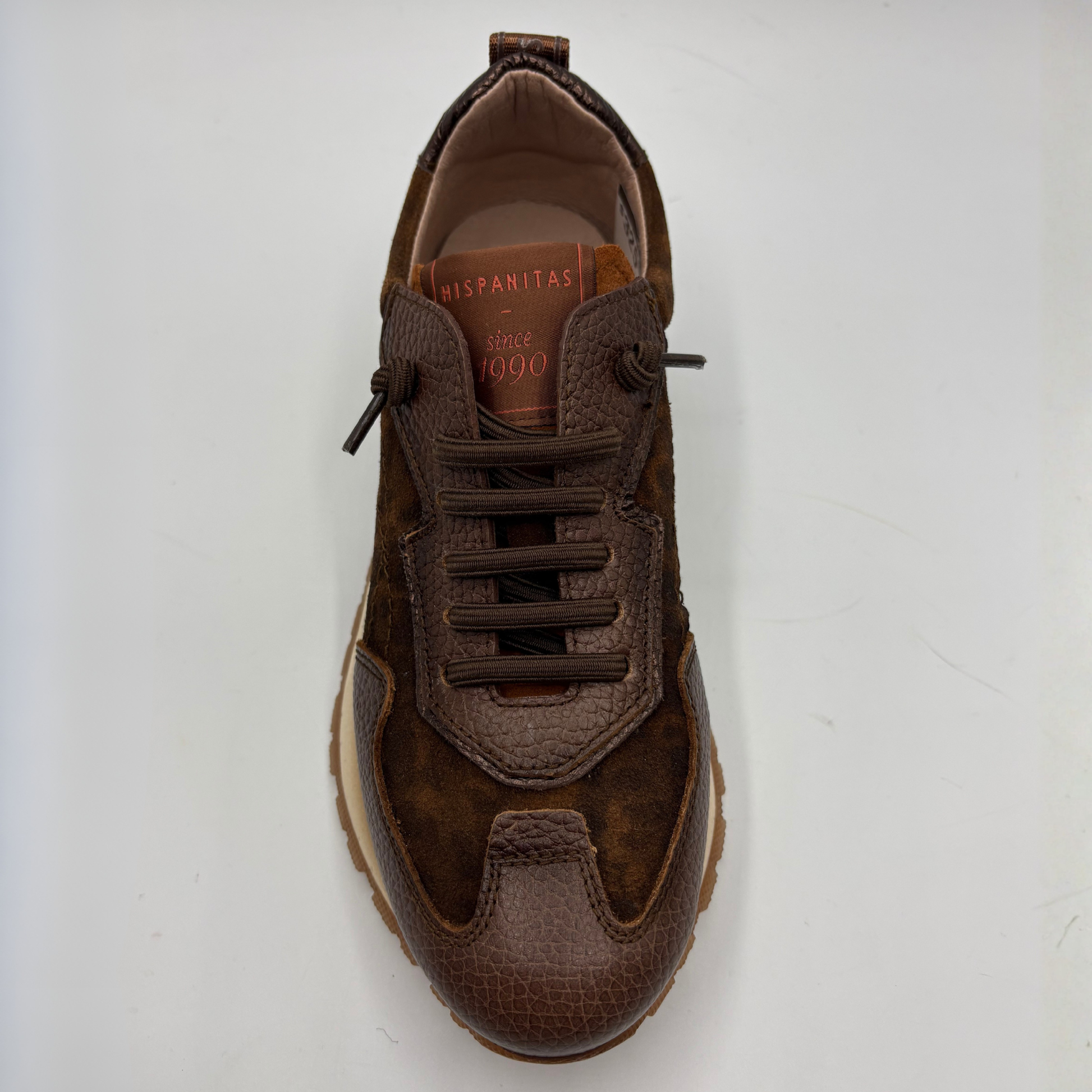 A brown suede and textured leather sneaker shown from a top-down view on a light gray background. The shoe features matching brown laces, a textured toe cap, and a tan interior lining with 'HISPANITAS' printed on the insole.