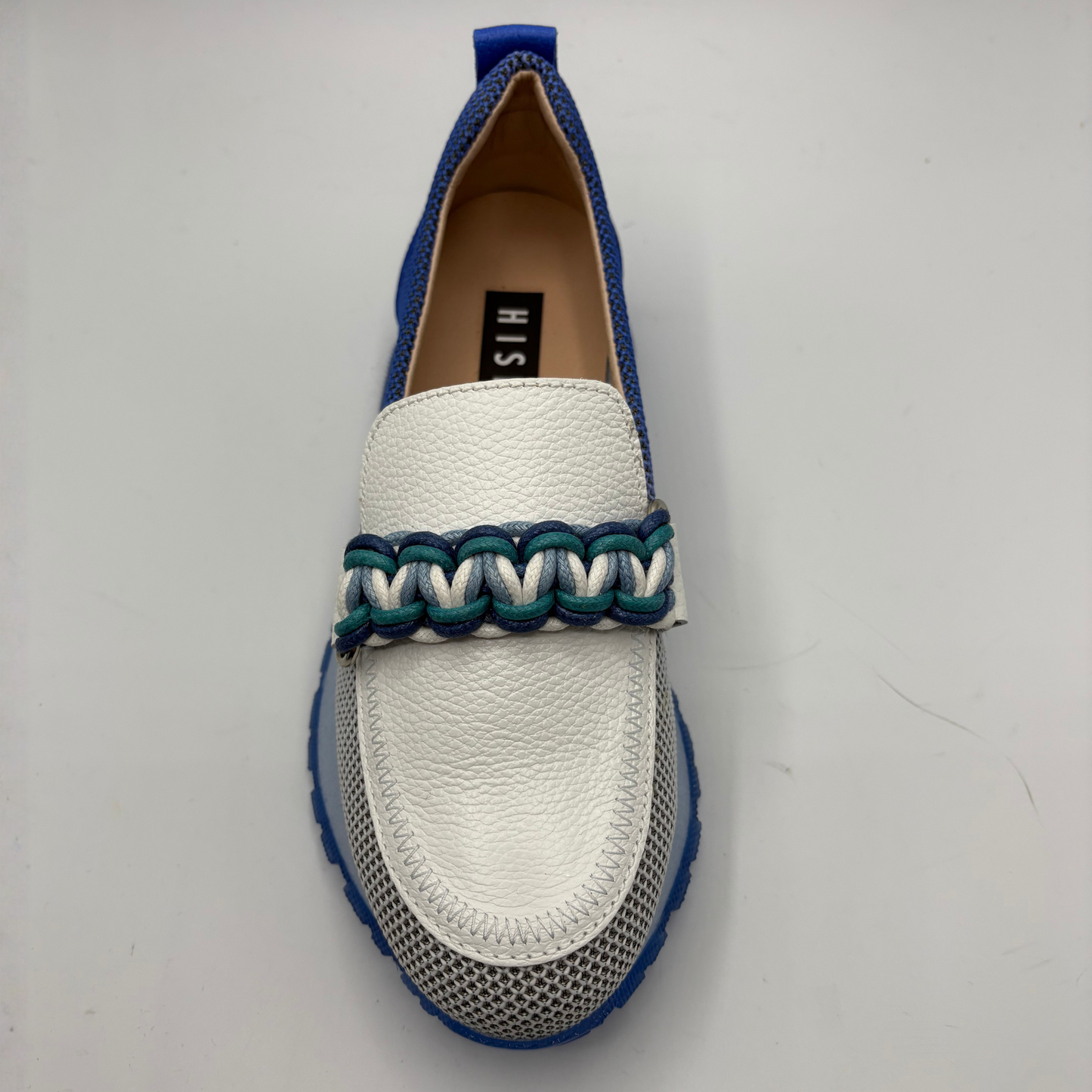 White loafer with blue and green braided detail on a light gray background