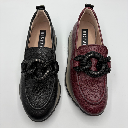 Two slip-on loafers with textured leather and a braided ring detail on the vamp, shown side by side on a light gray background. The left loafer is black, and the right loafer is burgundy.