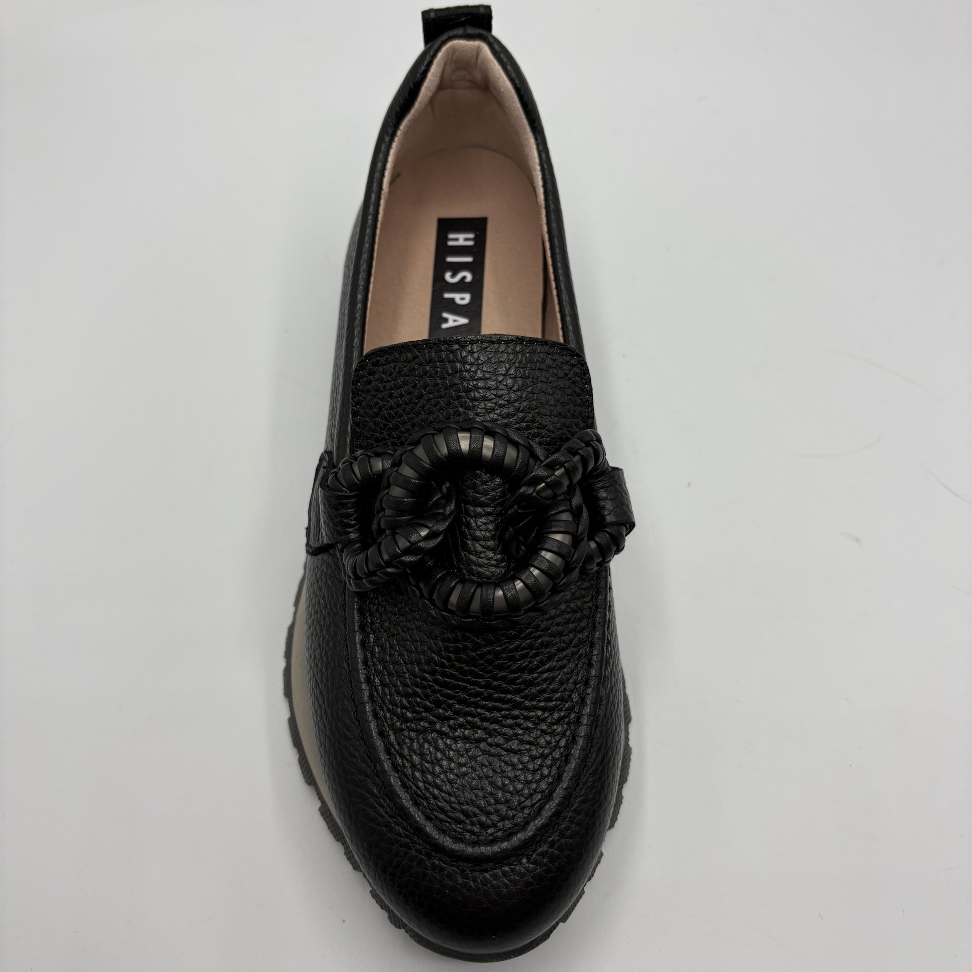 A black pebbled leather slip-on loafer with a braided rope detail across the vamp, photographed from a top-down angle on a light gray background. The insole features the brand name 'HISPANITAS’