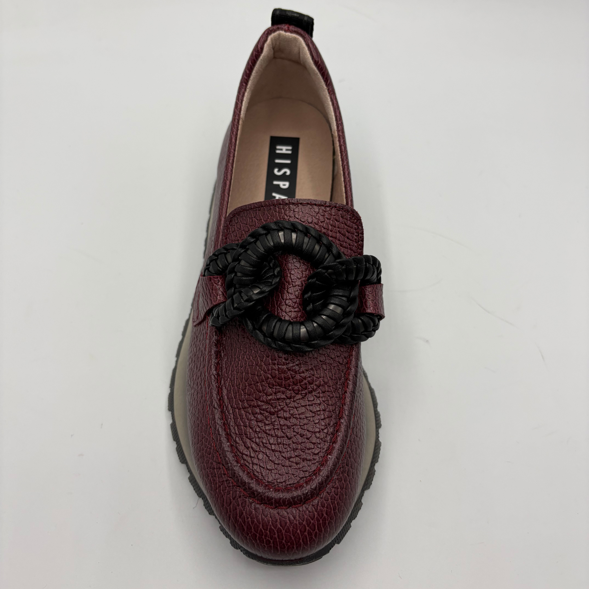 A burgundy pebbled leather loafer with a black braided rope detail across the vamp, photographed from a top-down angle on a white background. The insole features a black label with the brand name 'HISPANITAS’