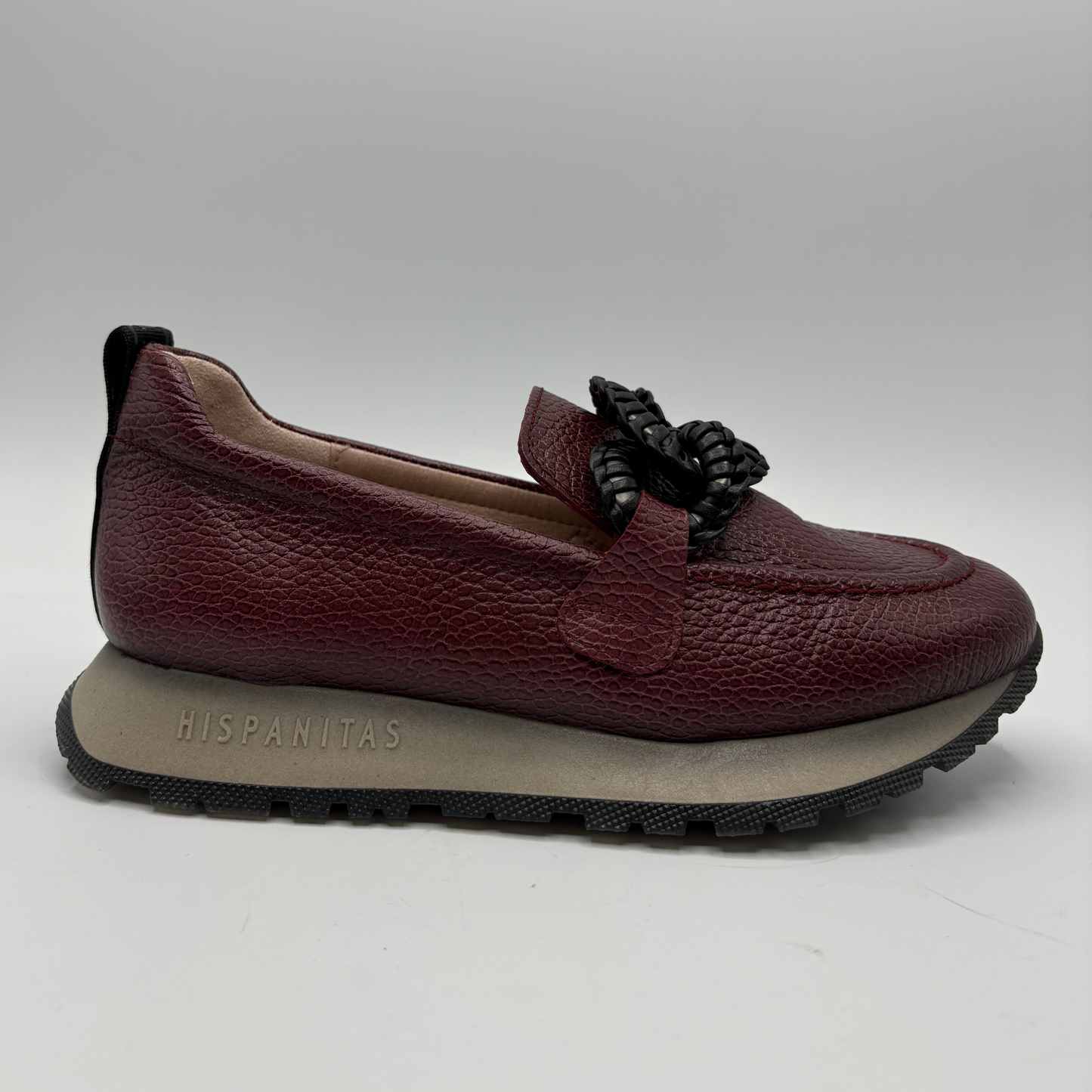 A burgundy pebbled leather slip-on loafer with a black braided detail on the vamp and a thick gray midsole embossed with 'HISPANITAS', shown against a neutral gray background.