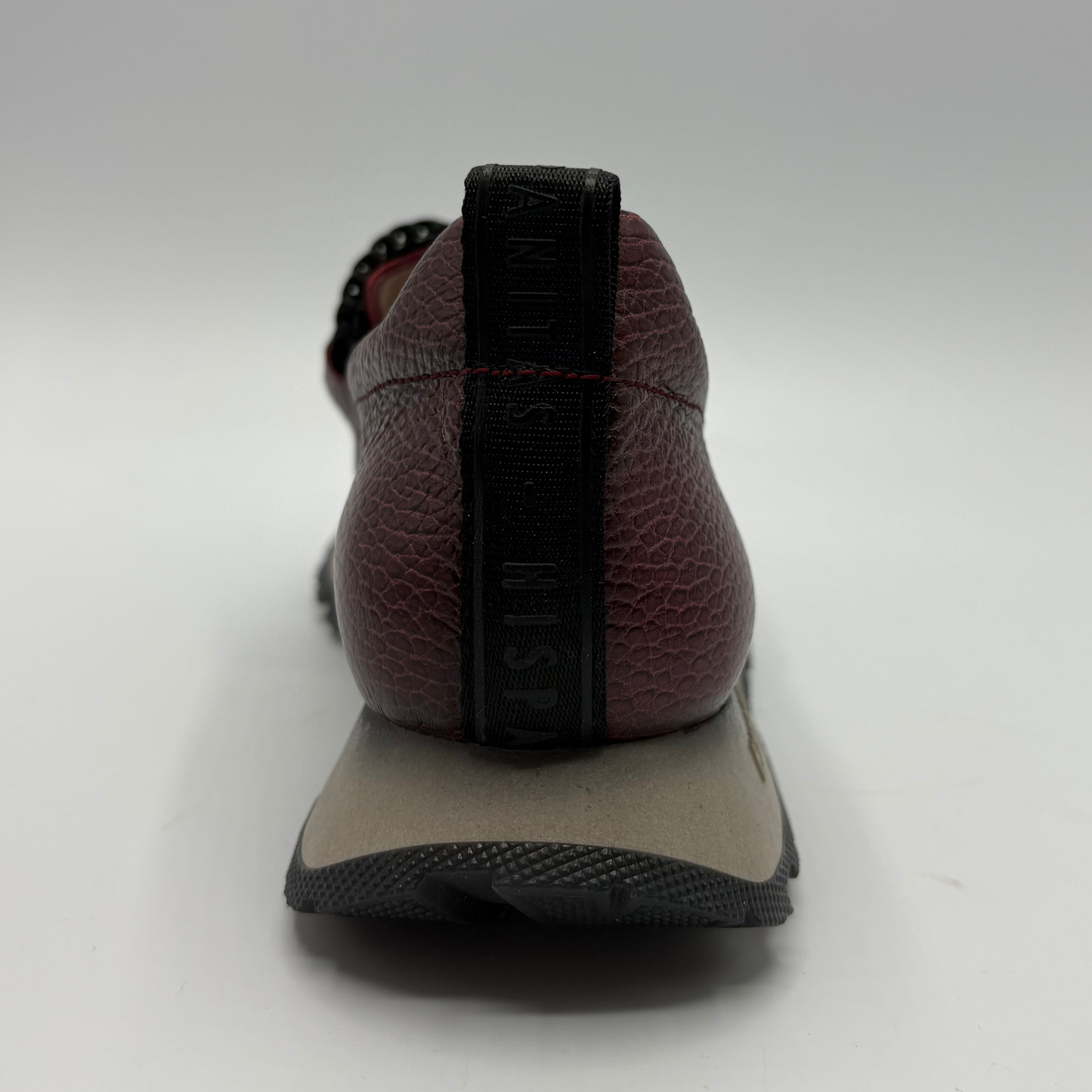 A close-up rear view of a Hispanitas loafer in burgundy pebbled leather with a black pull tab and a beige and black midsole.