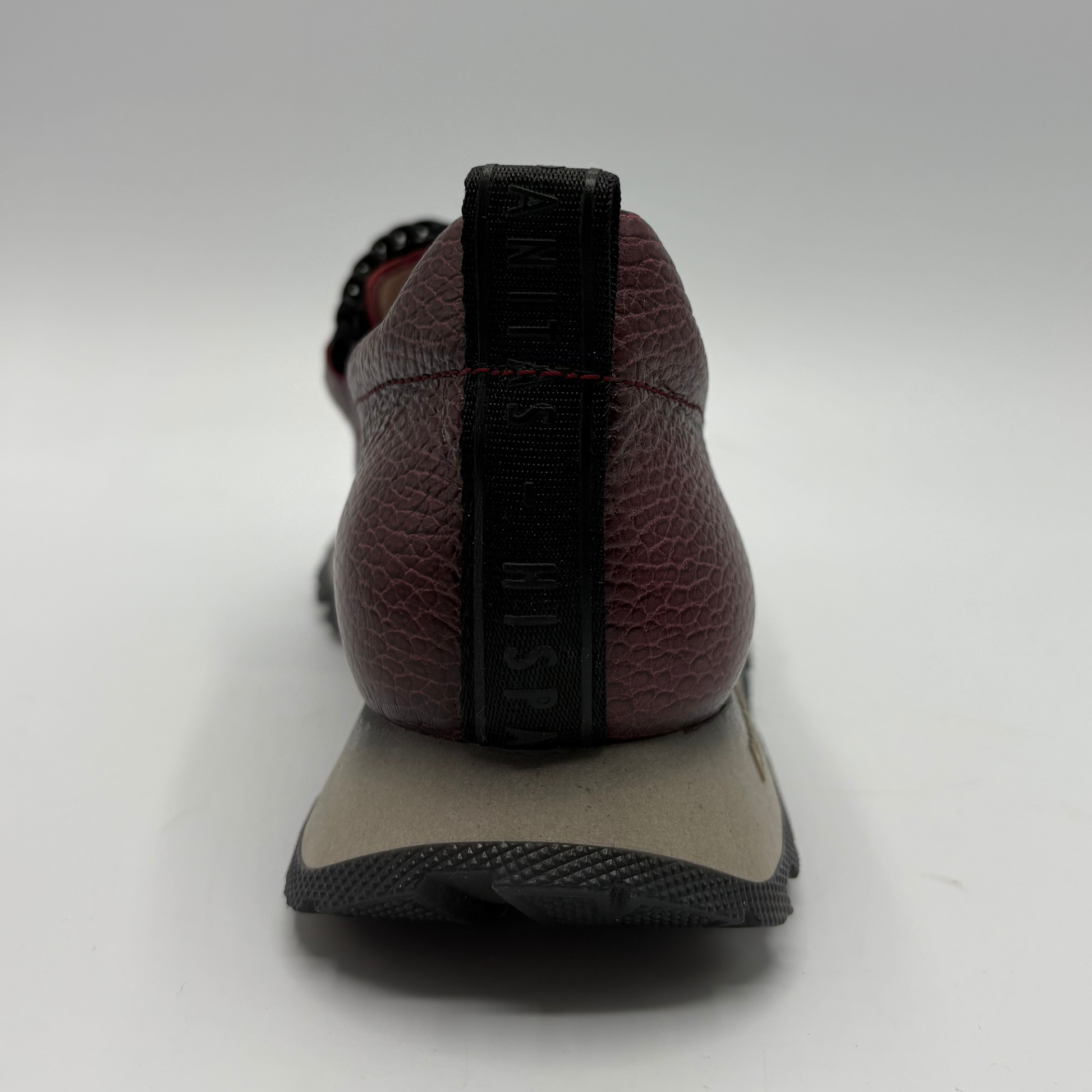 A close-up rear view of a Hispanitas loafer in burgundy pebbled leather with a black pull tab and a beige and black midsole.