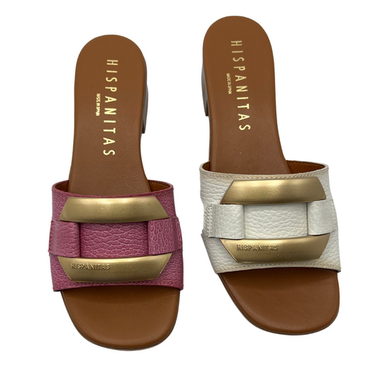 Top view of two mule sandals side by side, one pink and one white both with brown insoles and gold brooch detail on upper