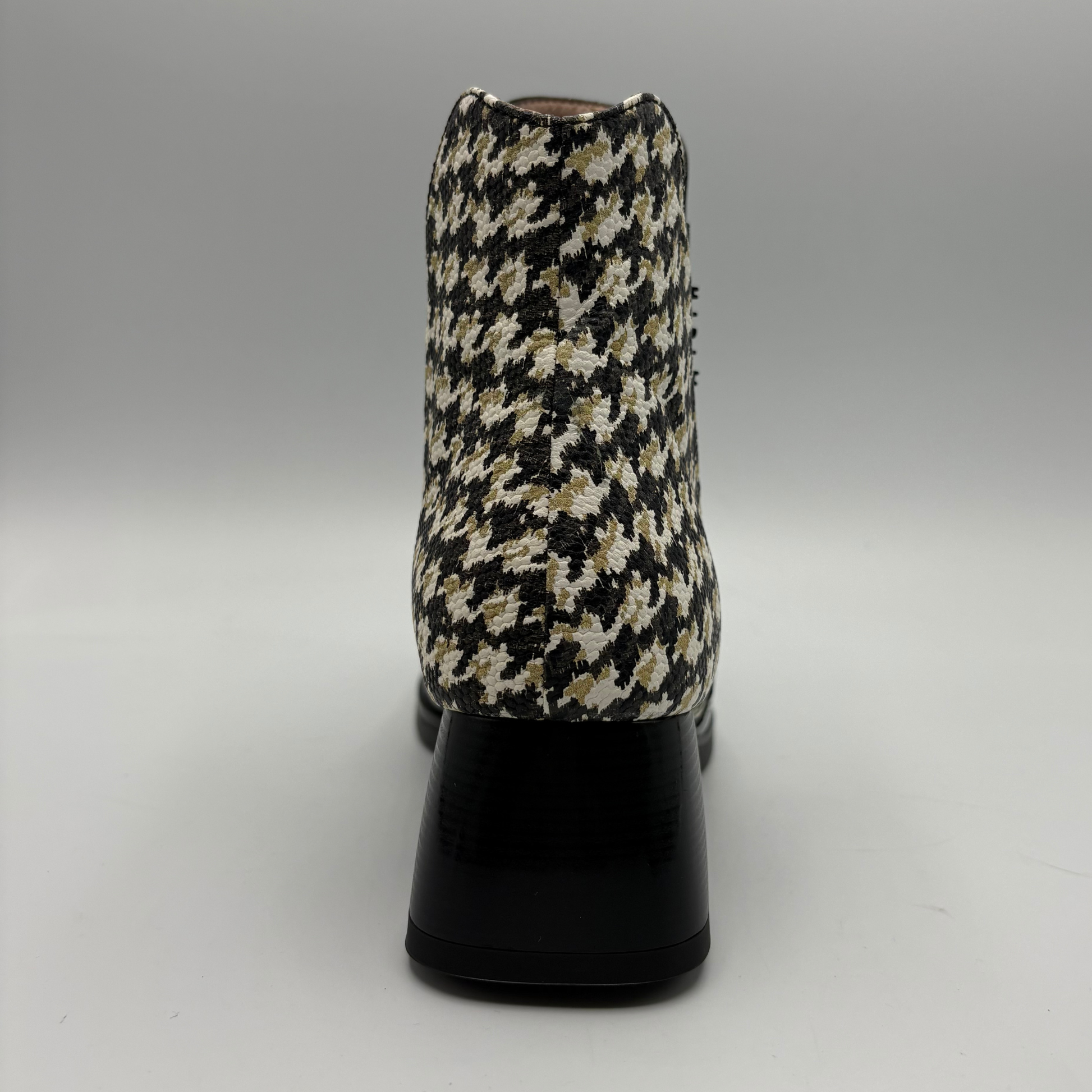 A single ankle boot shown from the back, featuring a black, beige, and white houndstooth patterned upper with a glossy black block heel, set against a neutral gray studio background.