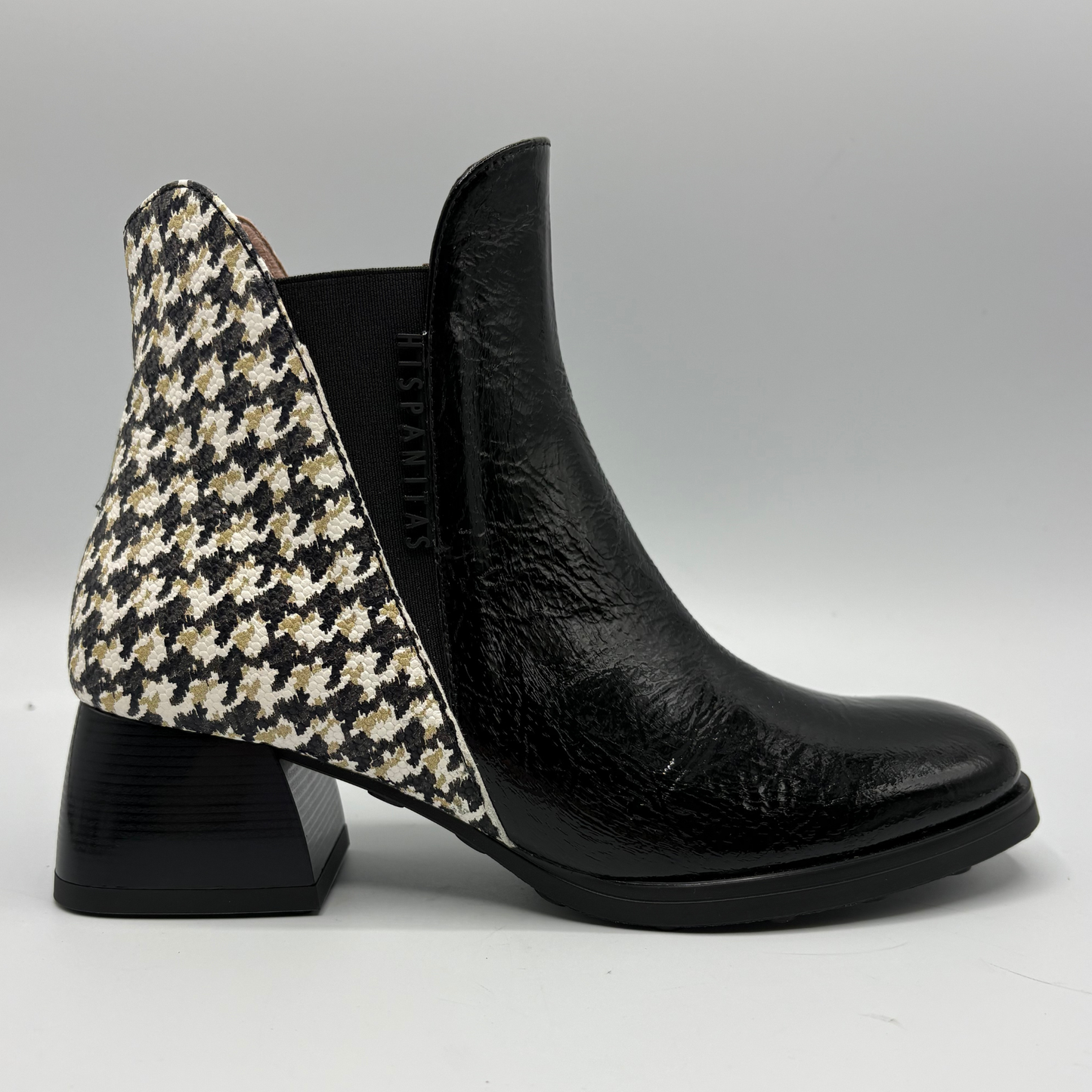 A black leather ankle boot with a black, beige, and white houndstooth patterned fabric heel counter, set against a neutral gray background.