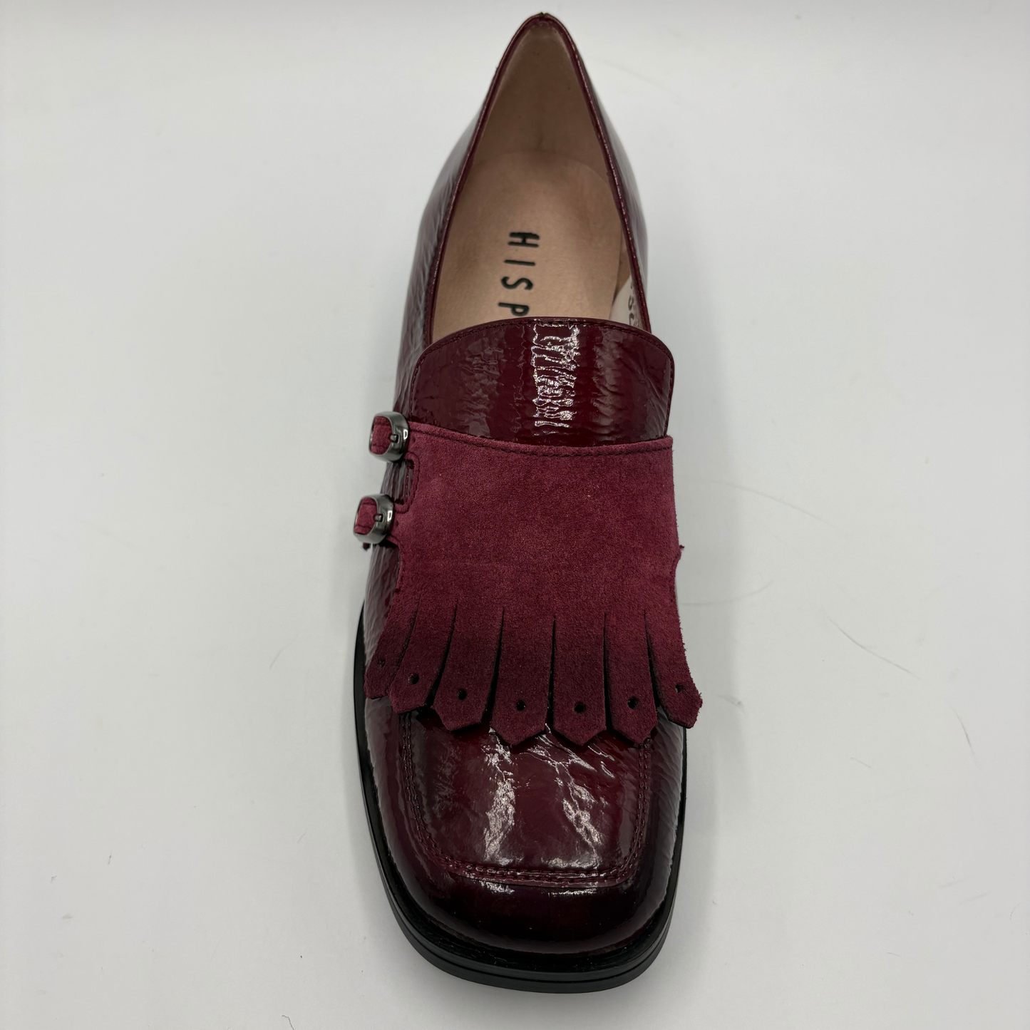 A single burgundy loafer with a glossy patent leather toe cap, a suede fringe strap across the instep, and a black sole, photographed from a top-down angle on a white background.