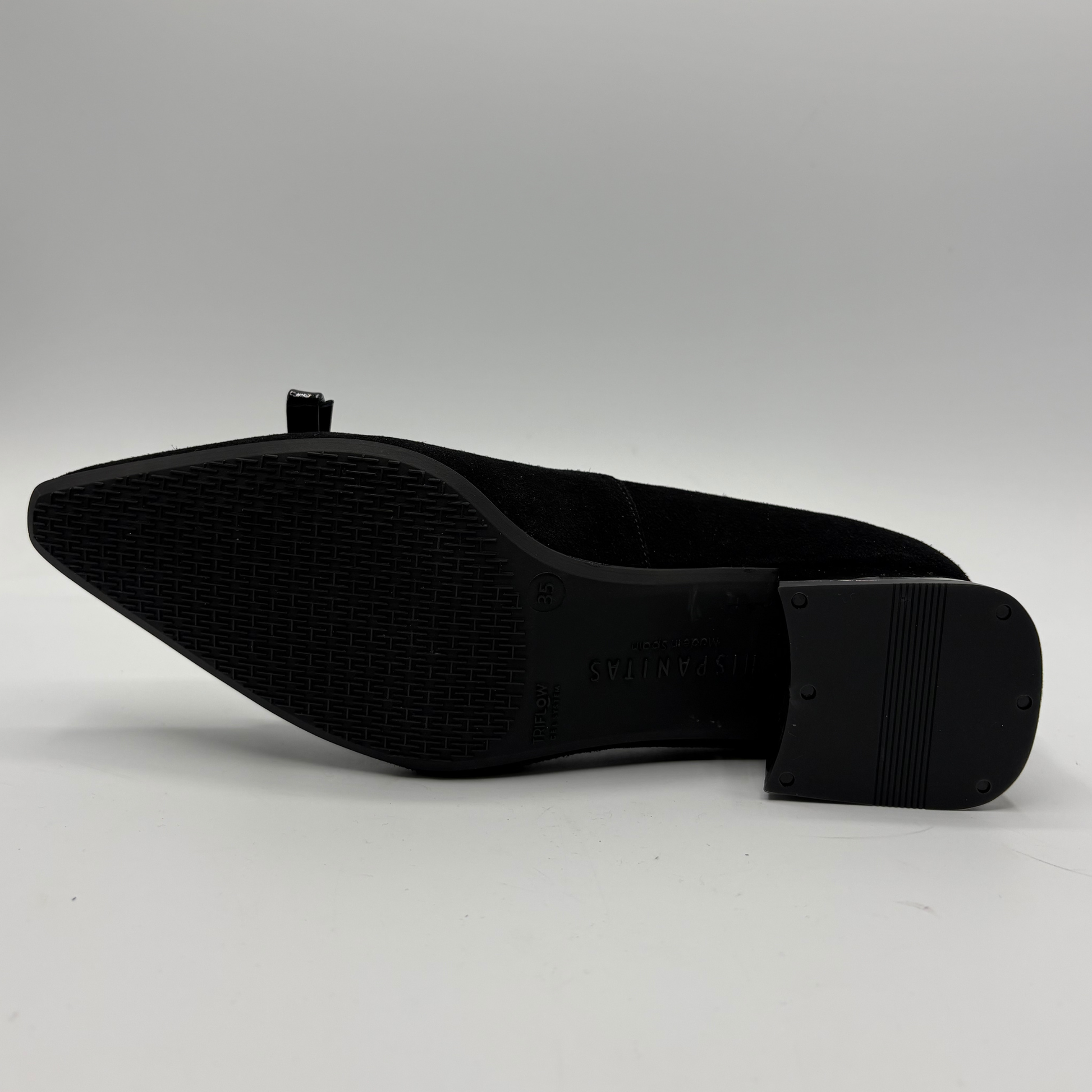A black pointed-toe shoe shown from the sole side, featuring a textured rubber outsole and a block heel, photographed on a light gray background.