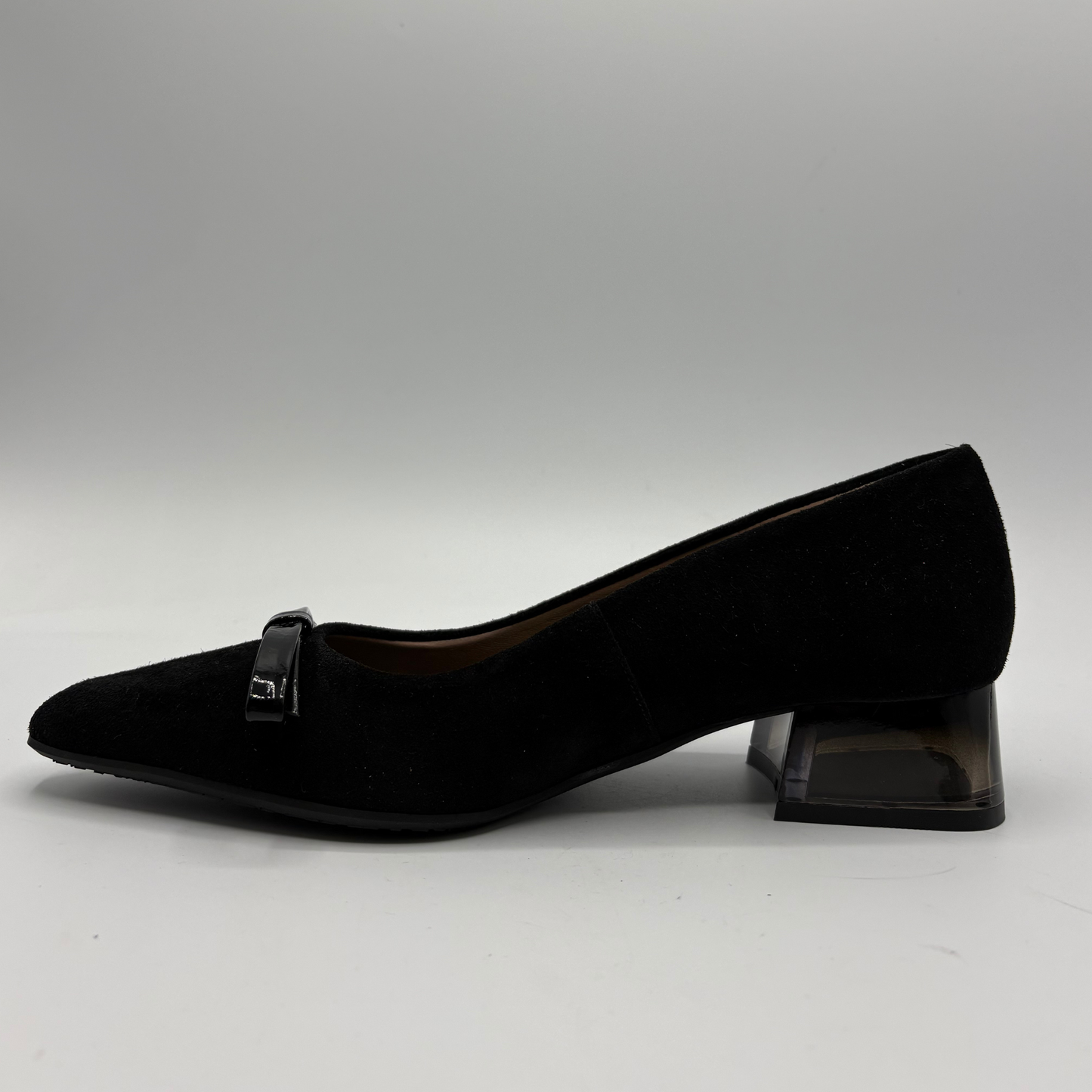 A single black pointed-toe pump shoe with a small bow detail on the strap, set against a neutral gray studio background.