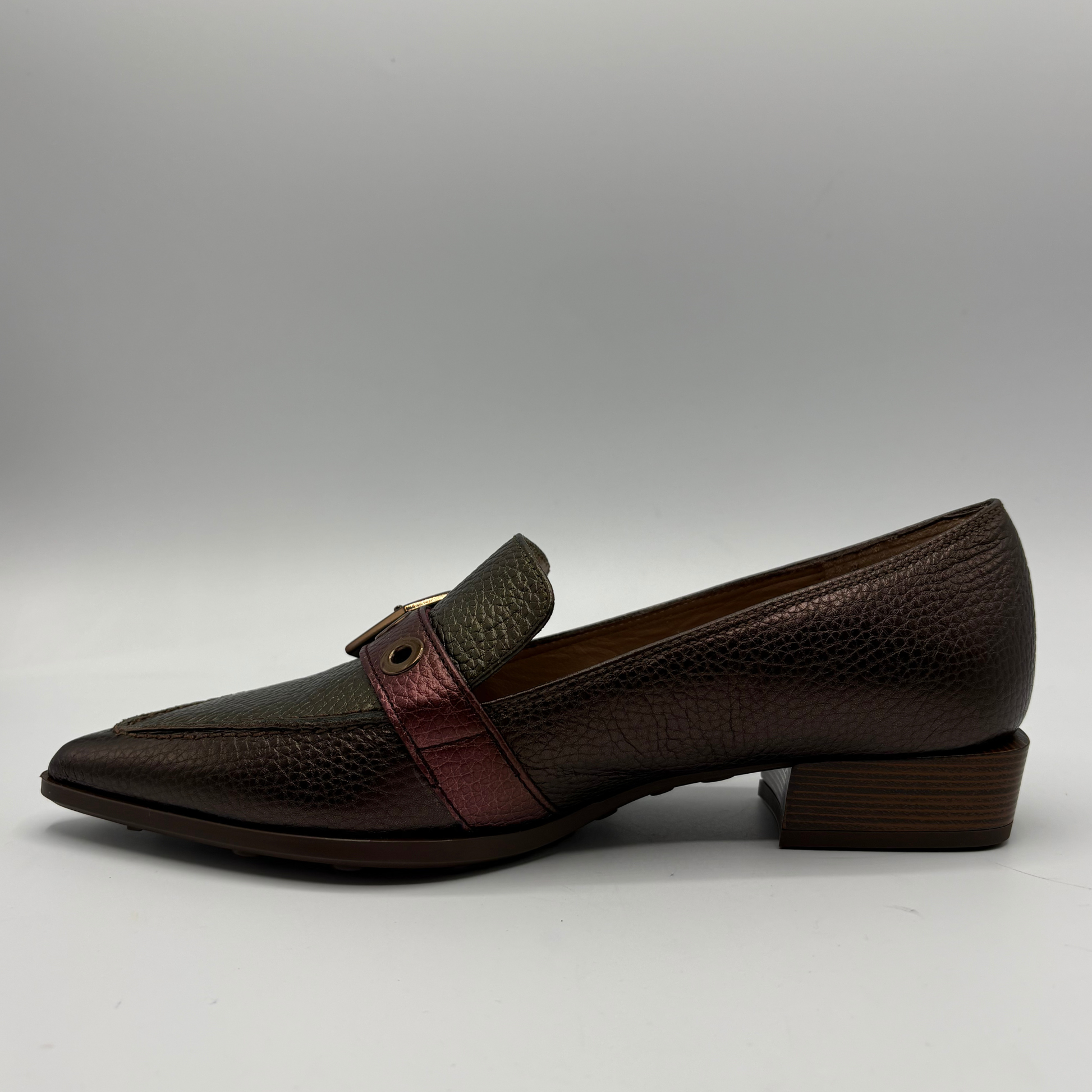 A dark brown pebbled leather loafer with a pointed toe, a low stacked heel, and a burgundy leather strap across the instep with a small gold-tone buckle.