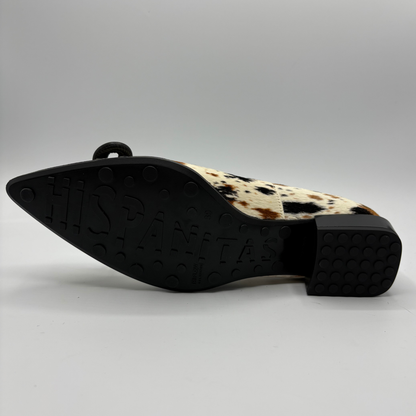 A single pointed-toe flat shoe shown from the side, featuring a black sole with 'HISPANITAS' embossed in large letters and a cream and brown cowhide-patterned upper.