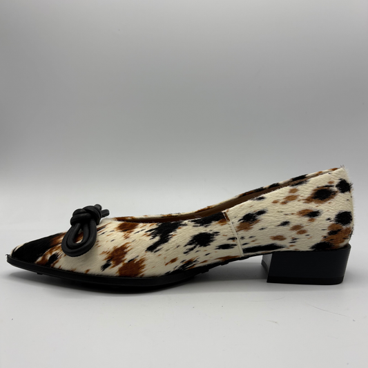 A single women's low-heel pump shoe featuring a brown, black, and cream cowhide pattern, finished with a black pointed toe and a black knotted bow detail on the vamp.