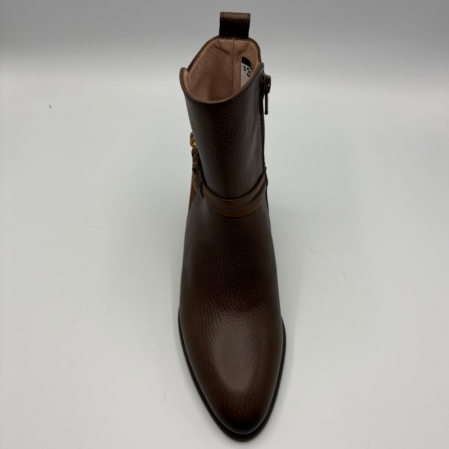 A dark brown pebbled leather ankle boot with a side buckle strap, shown from a front-facing perspective on a light gray background.