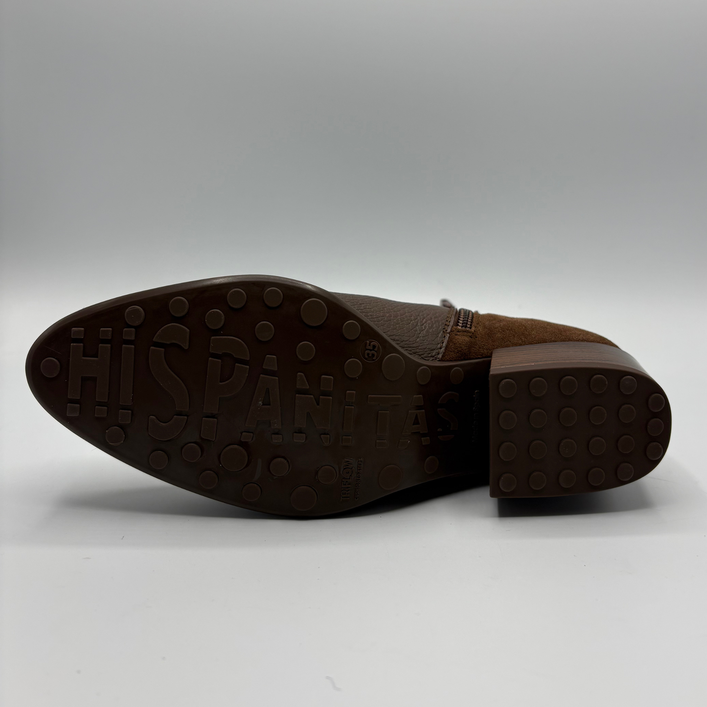 A brown suede boot shown from the sole side, featuring a dark brown rubber outsole with 'HISPANITAS' embossed in large letters and a block heel.