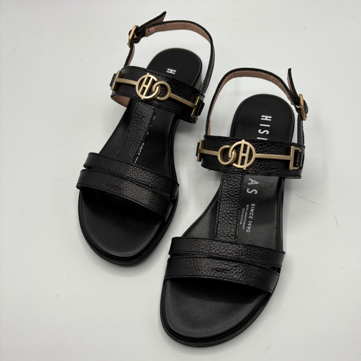 Black sandals with gold accents on a white background