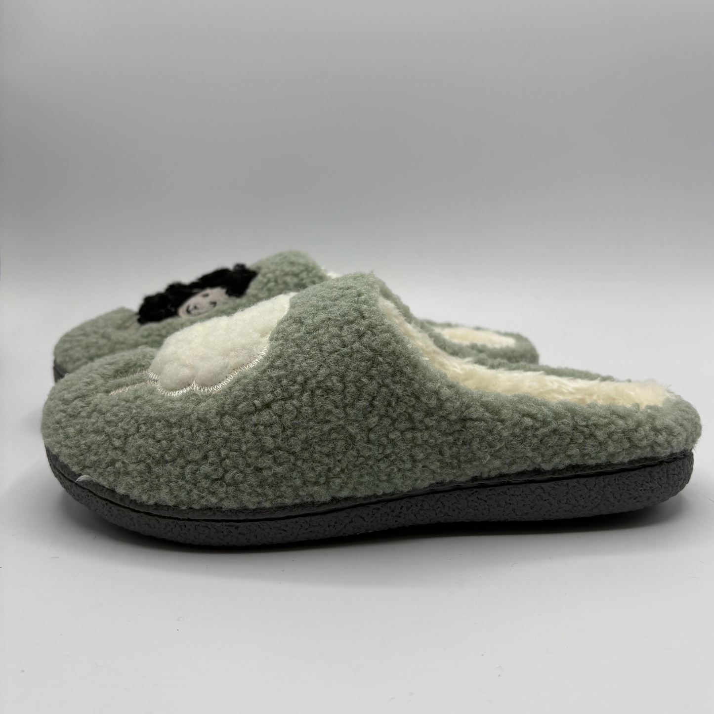 Left view of a plush fleece slip-on slippers in sage green, featuring a cream sherpa lining, with a white sheep detail on the toe box