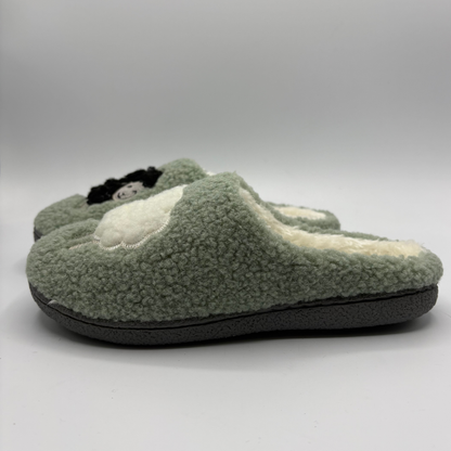 Left view of a plush fleece slip-on slippers in sage green, featuring a cream sherpa lining, with a white sheep detail on the toe box
