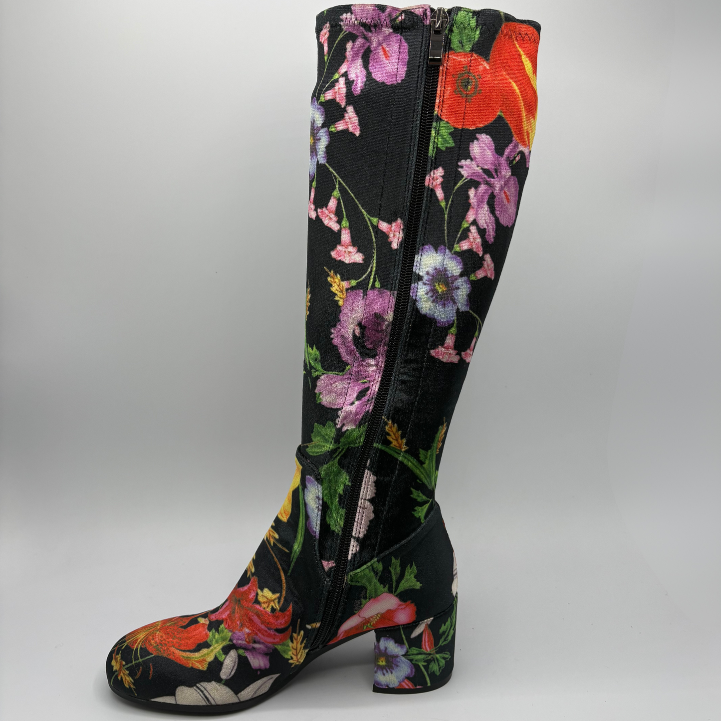A single knee-high boot with a black base and a vibrant, multicolored floral print featuring pink, red, purple, and green flowers, shown against a neutral gray background.