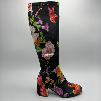 A single knee-high boot with a black base and a vibrant, multicolored floral print featuring pink, red, purple, and green flowers, shown against a neutral gray background.