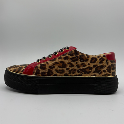 A low-top platform sneaker featuring a brown and black leopard print upper, red patent leather side panels, a gold zipper, and a thick black platform sole.