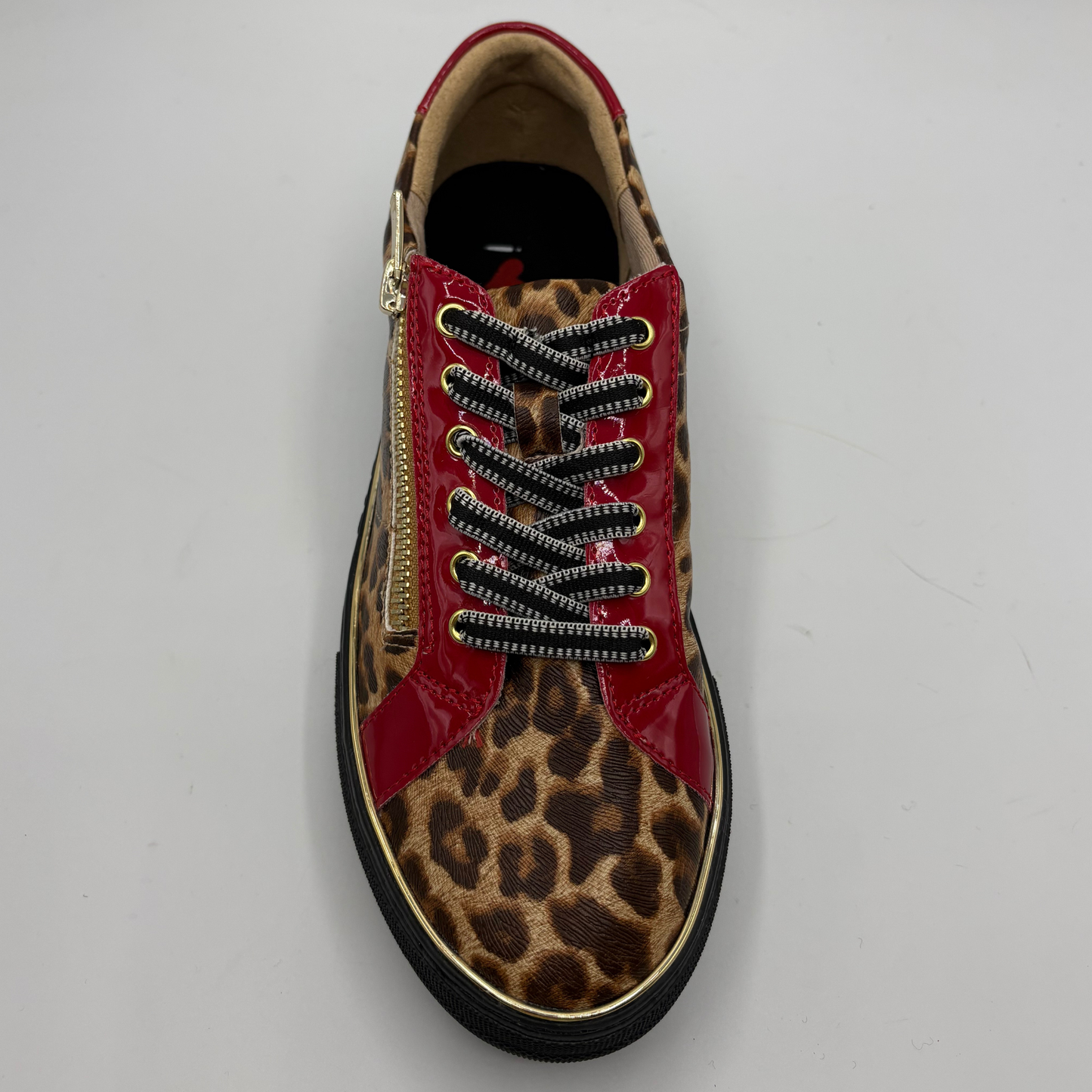 A single low-top sneaker shown from a top-down view on a light gray background. The shoe features a leopard print pattern on the toe and quarter panels, glossy red patent leather side panels, black and white patterned laces, a gold zipper on the side, and a black sole with a thin gold trim.
