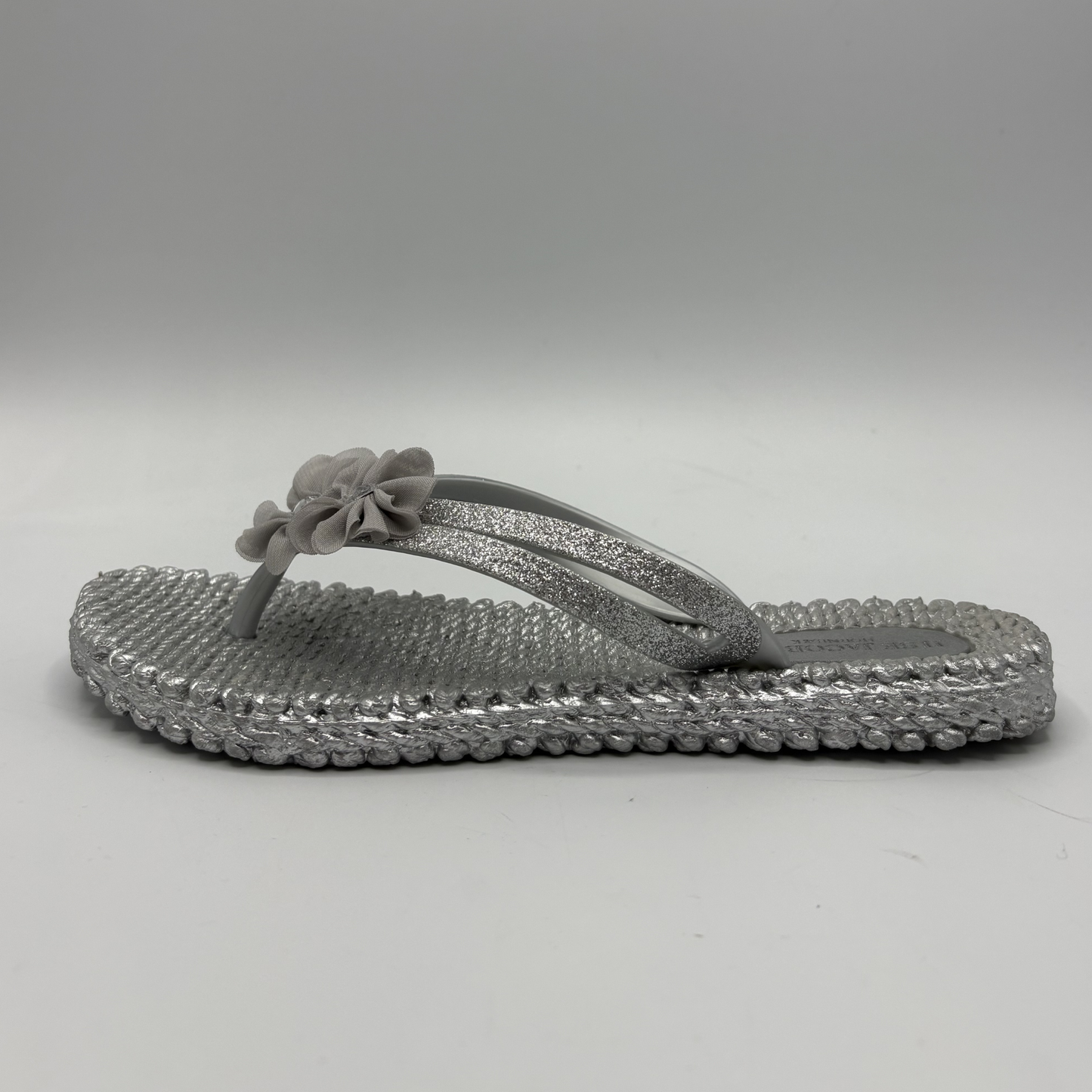 Left facing view of a silver flip flop with flower accents