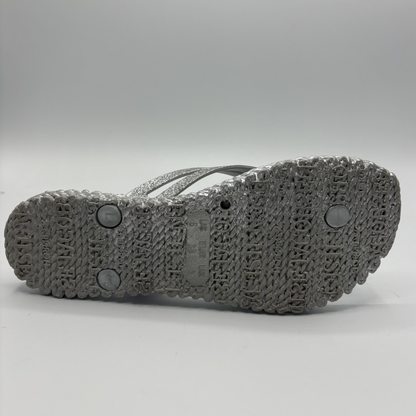 Bottom view of a silver flip flop with flower accents