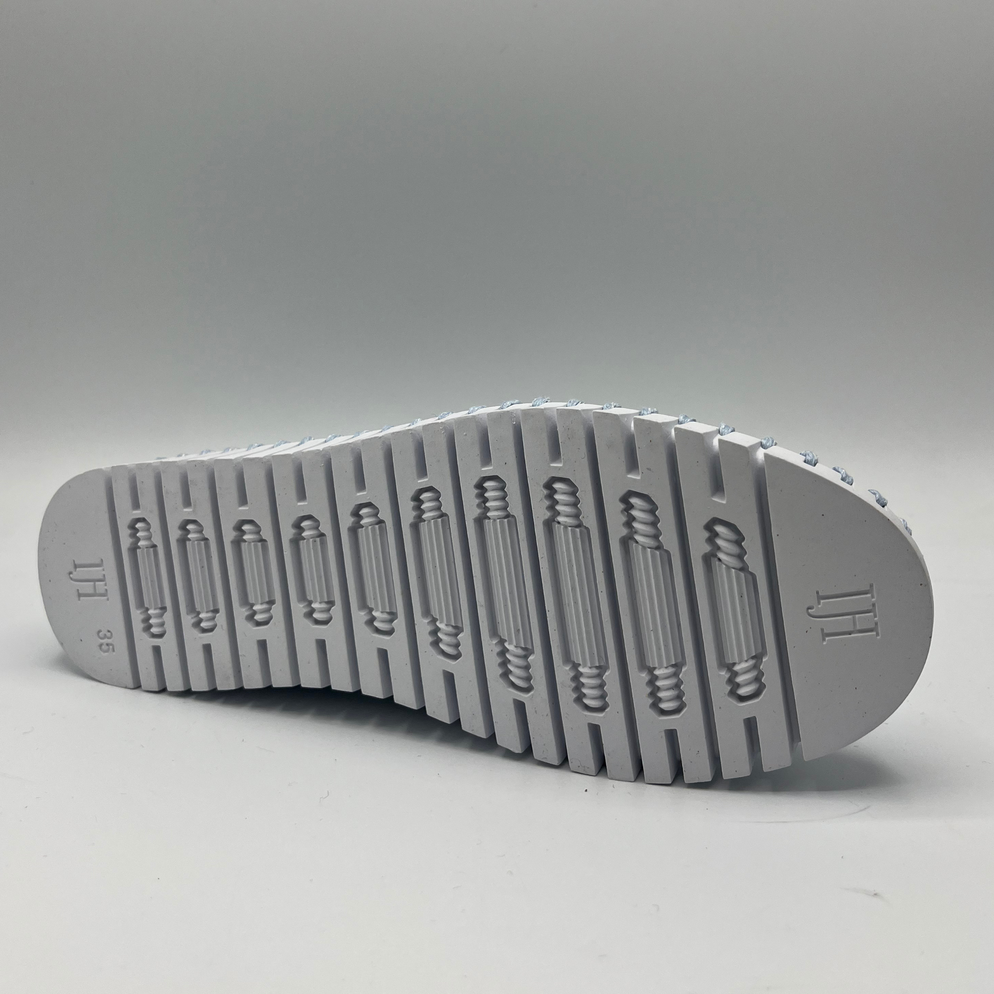 Bottom view of ash blue slip on shoe with an intricate laser cut upper and white rubber outsole.