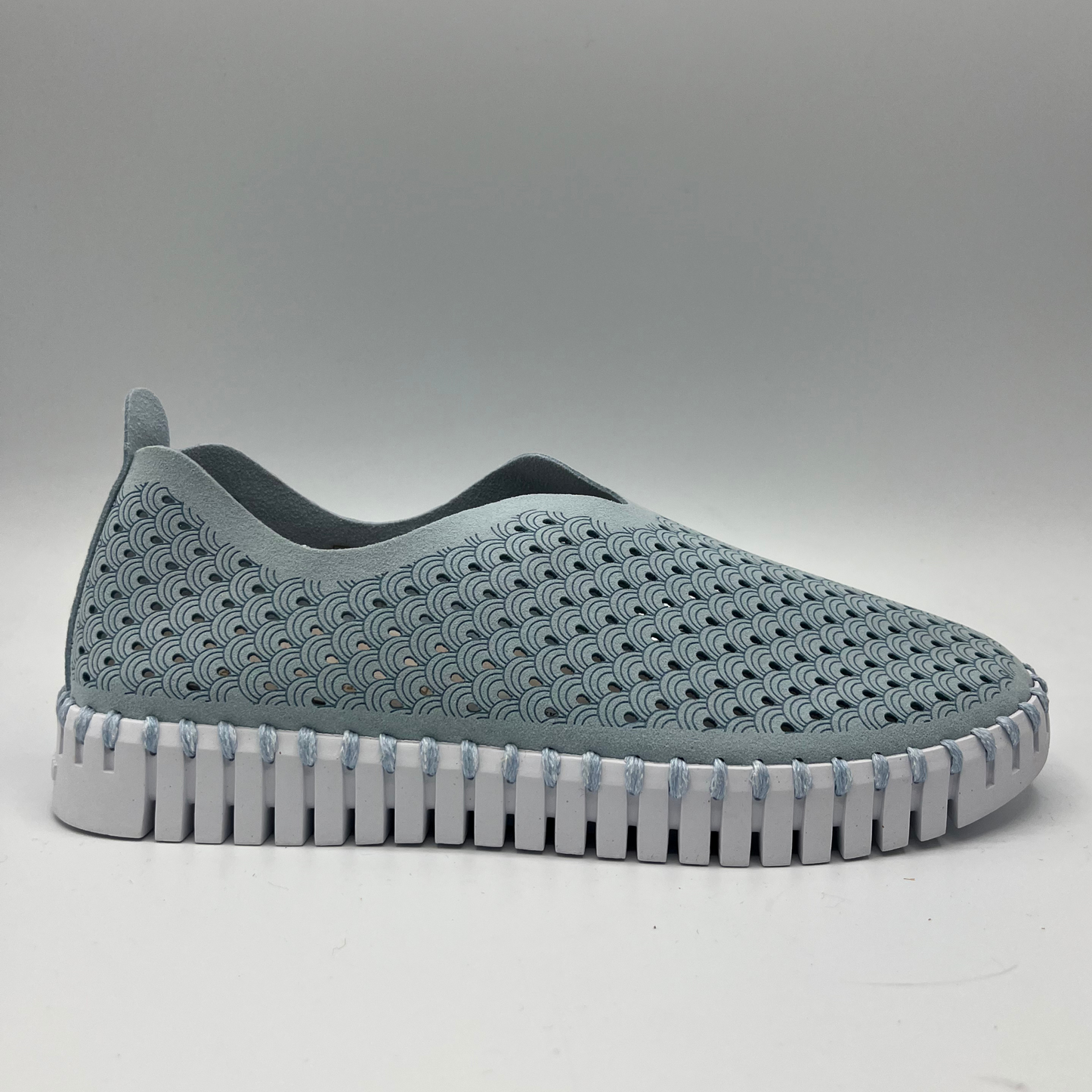 Right facing view of ash blue slip on shoe with an intricate laser cut upper and white rubber outsole.