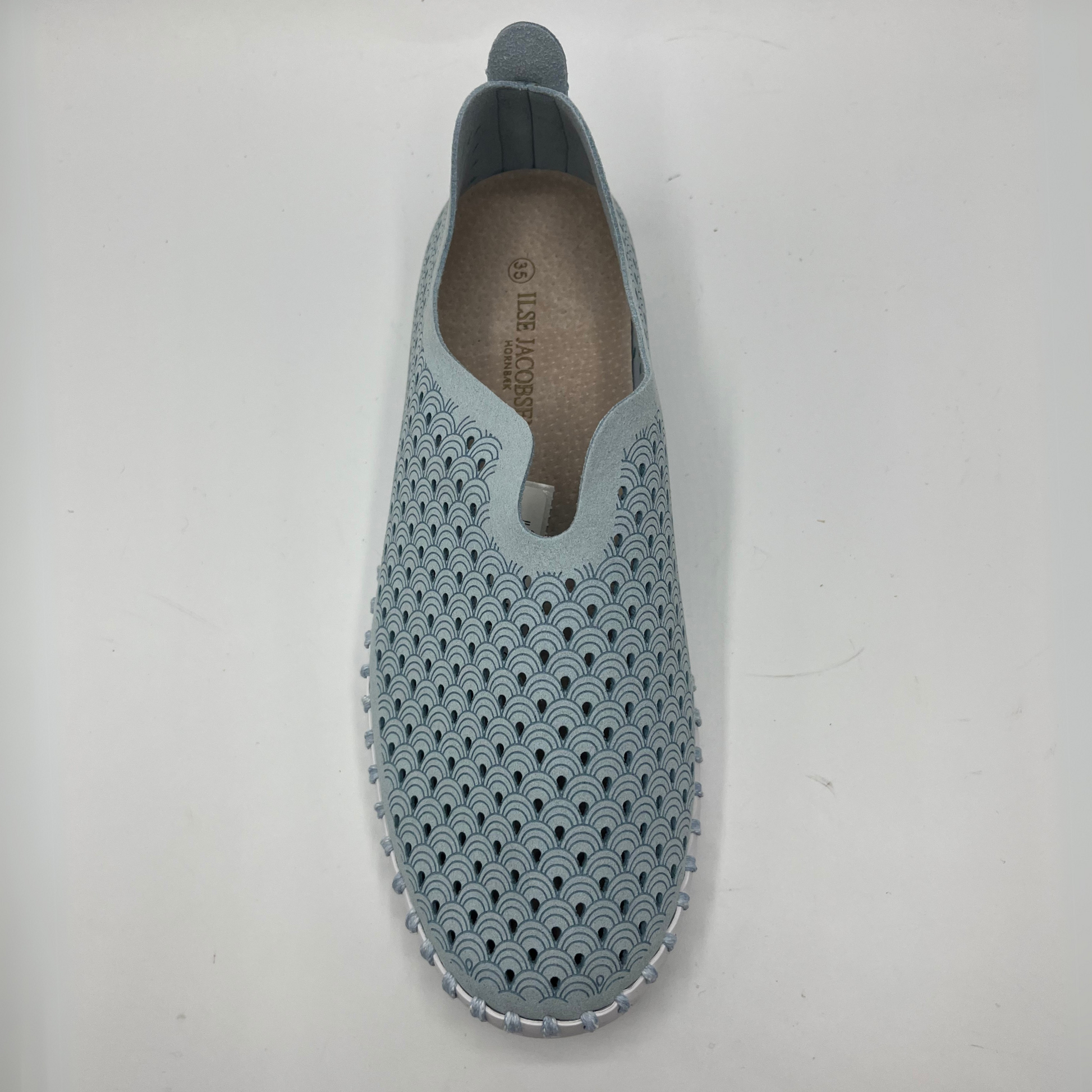 Top facing view of ash blue slip on shoe with an intricate laser cut upper and white rubber outsole.