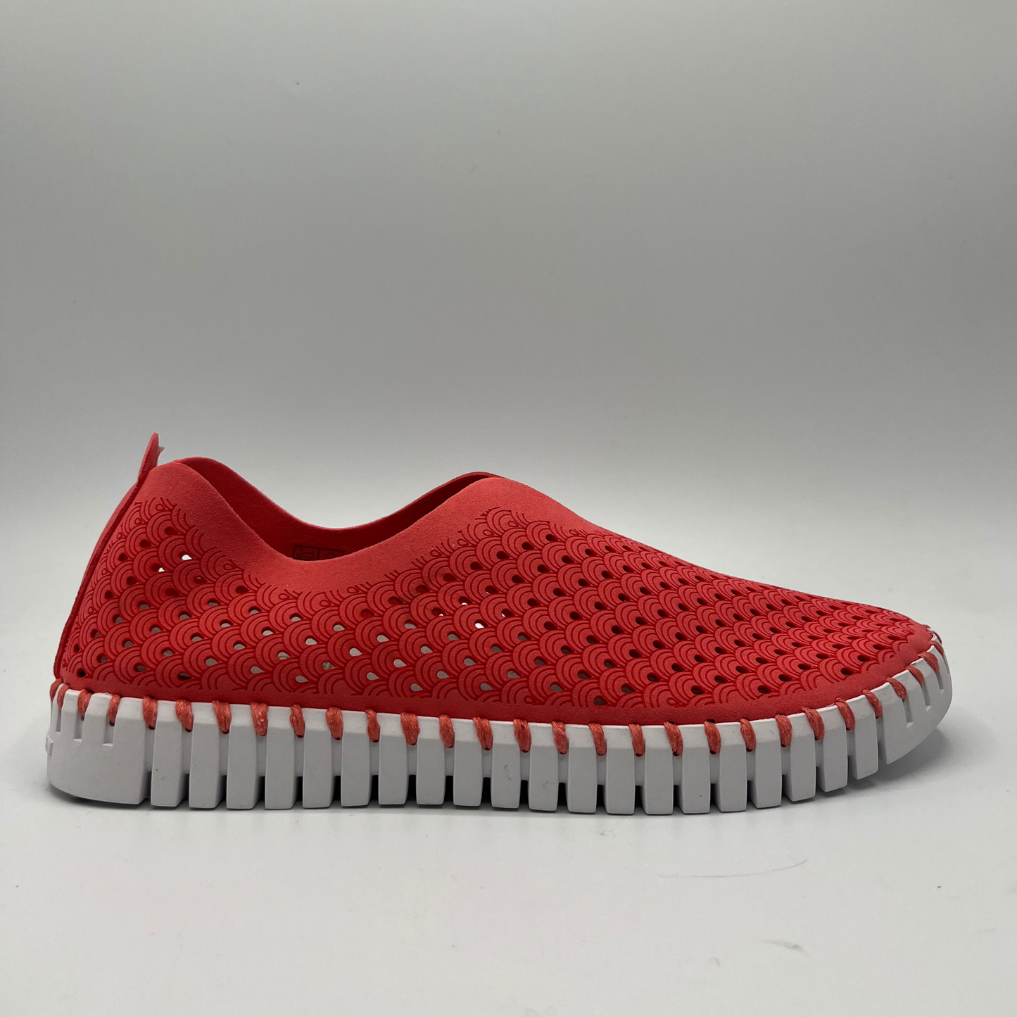 Right facing view of raspberry coloured slip on shoe with an intricate laser cut upper and white rubber outsole.