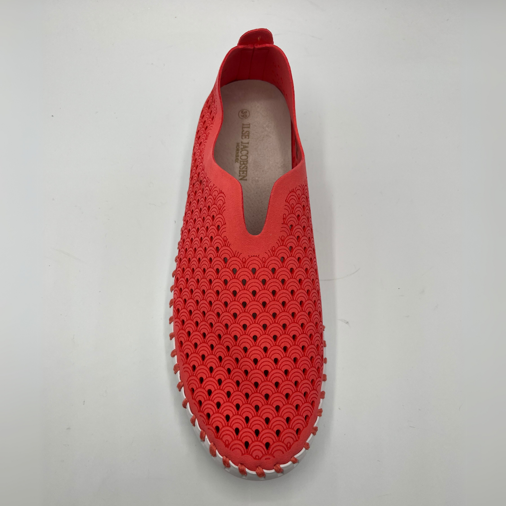 Top view of raspberry coloured slip on shoe with an intricate laser cut upper and white rubber outsole.