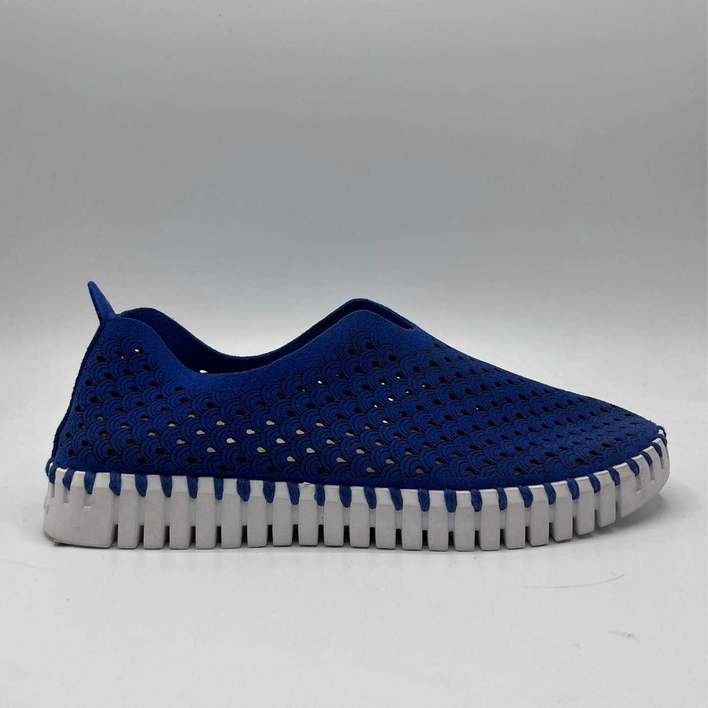 Right facing view of blue slip on shoe with an intricate laser cut upper and white rubber outsole.