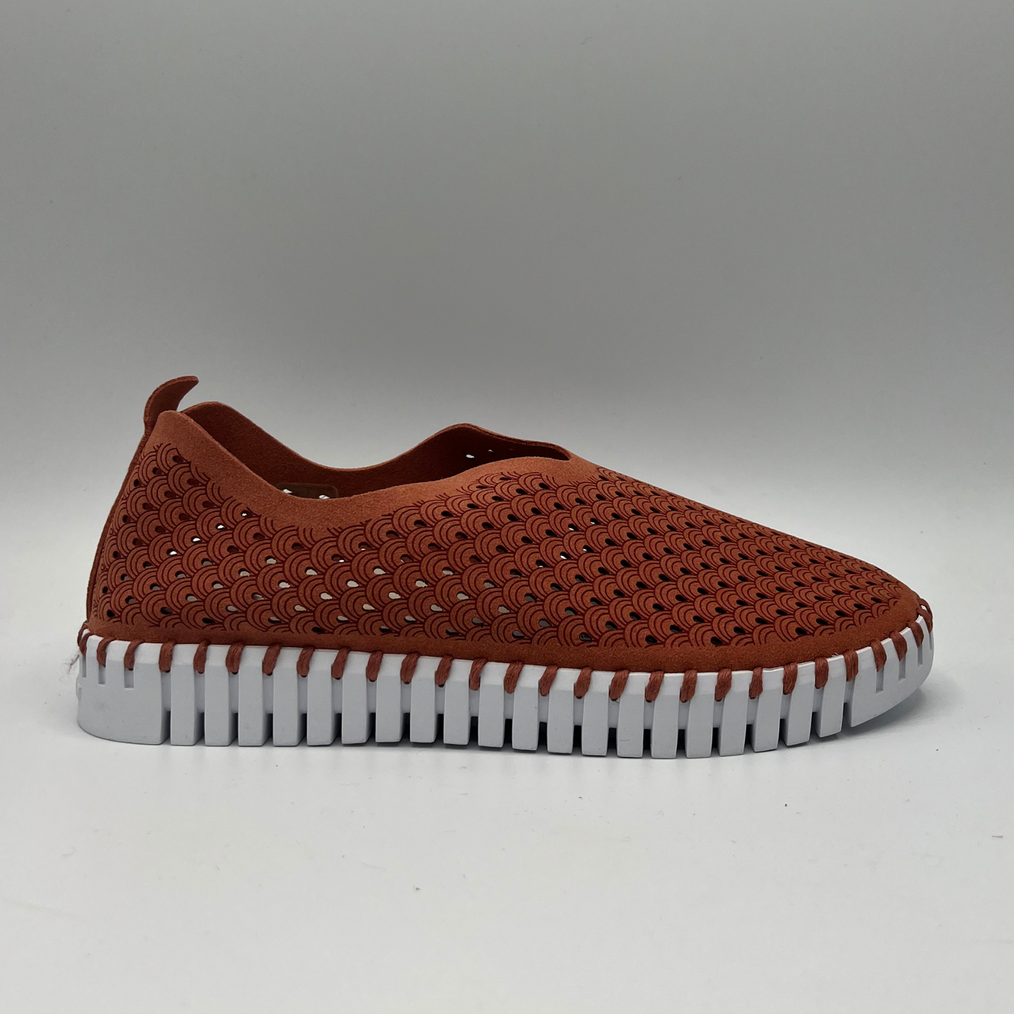 Right facing view of brick coloured slip on shoe with an intricate laser cut upper and white rubber outsole.