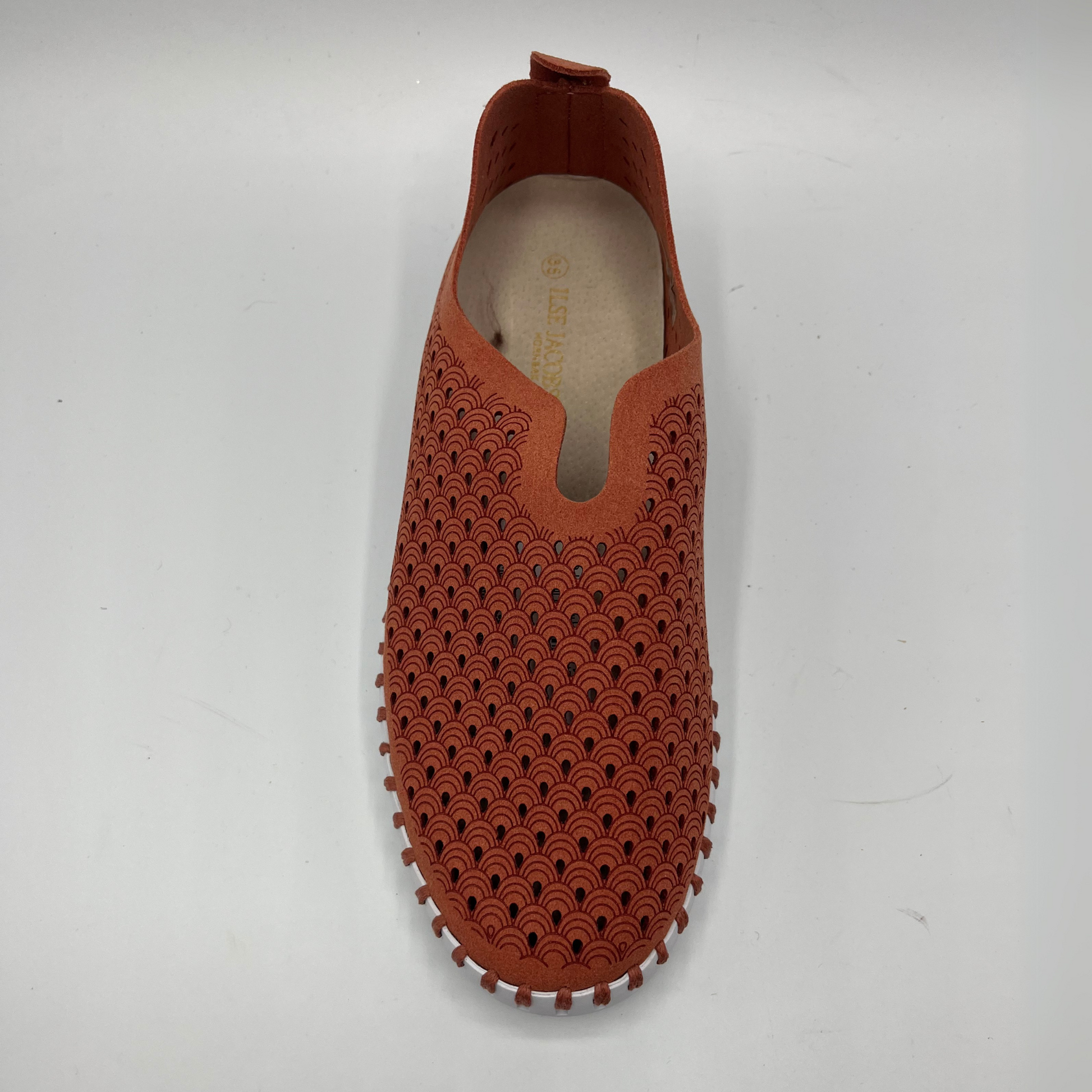 Top view of brick coloured slip on shoe with an intricate laser cut upper and white rubber outsole.