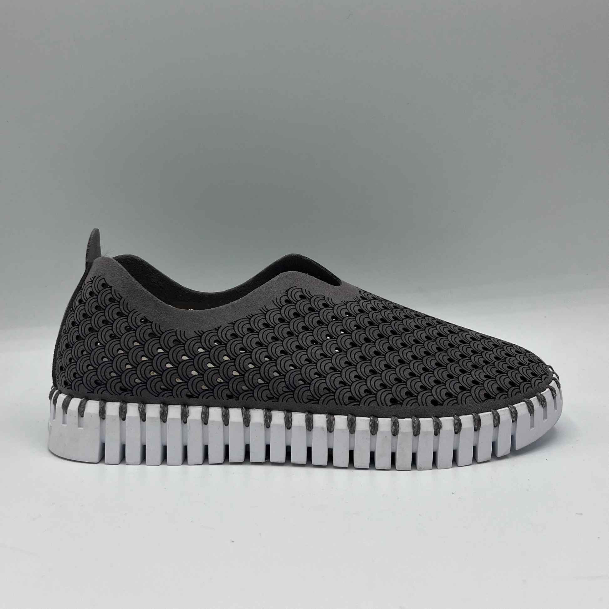 Right facing view of grey smoked pearl slip on shoe with an intricate laser cut upper and white rubber outsole.