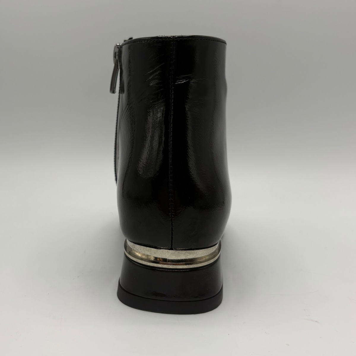 A black patent leather ankle boot shown from the back, featuring a silver metallic ring accent around the base of the block heel.